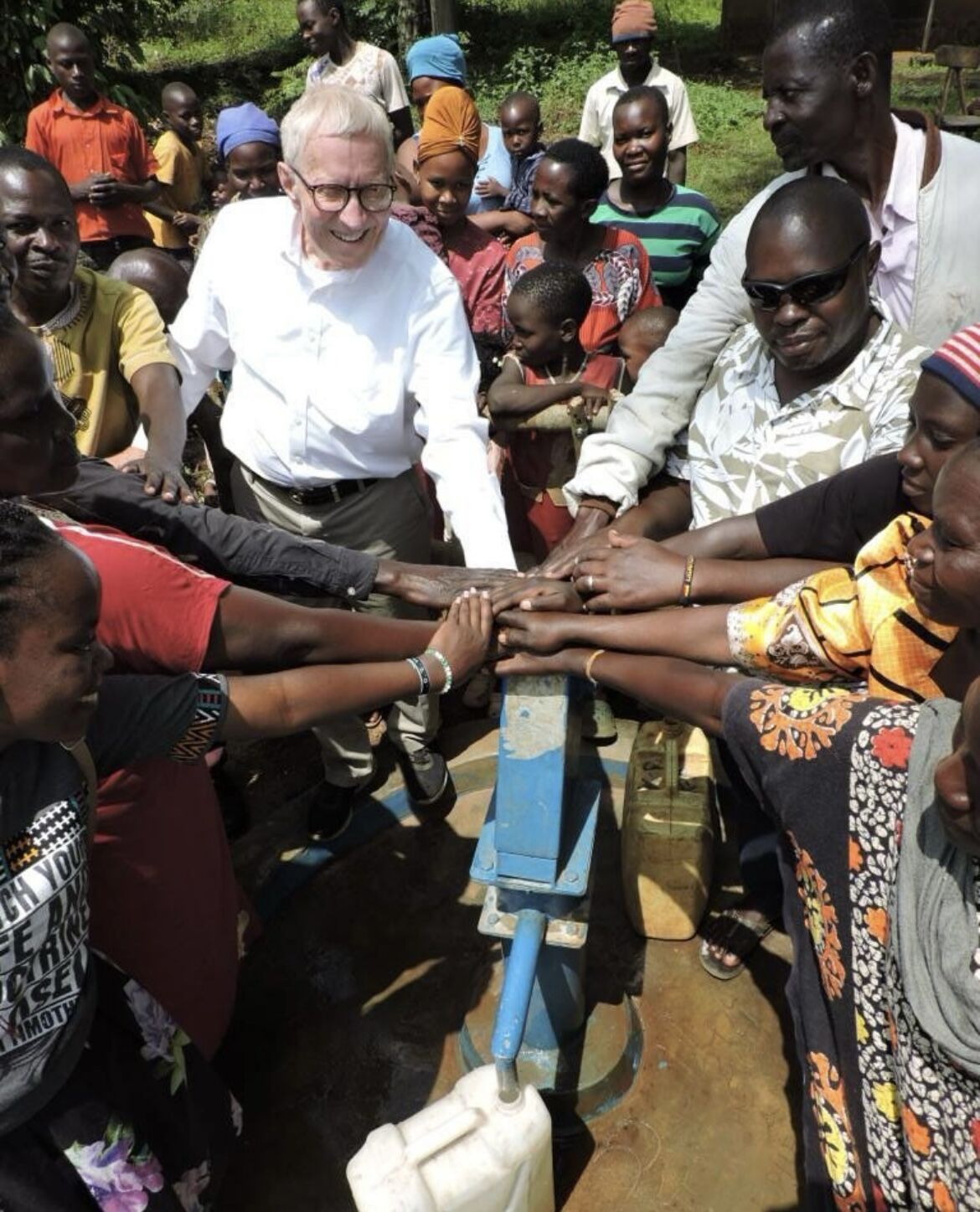 John Womack and community members with hands joined over a newly working well